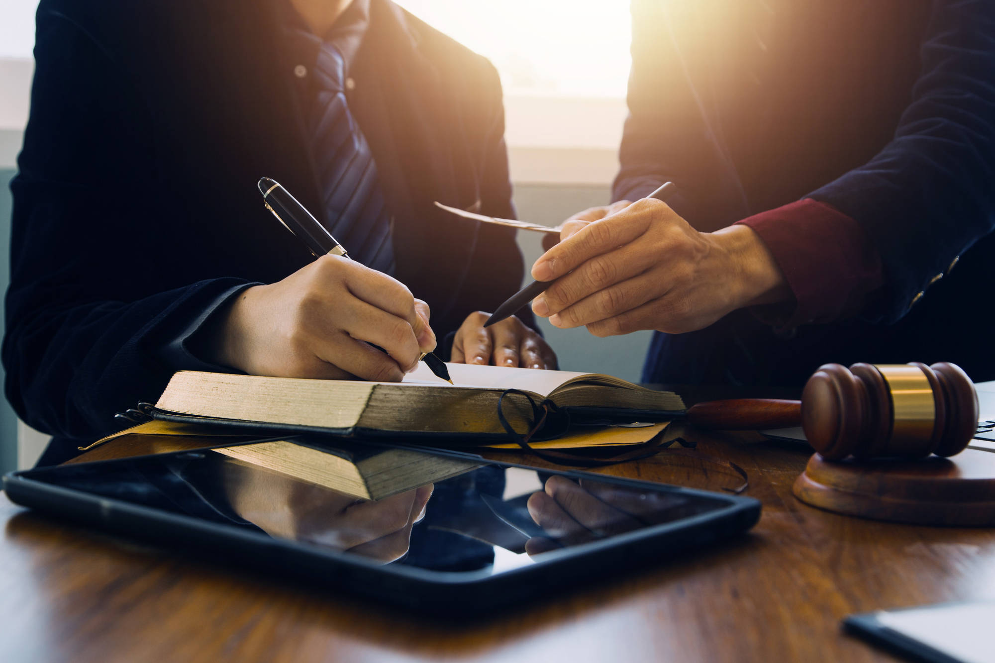 Two lawyers using pens to point at an entry in a book on a wooden table