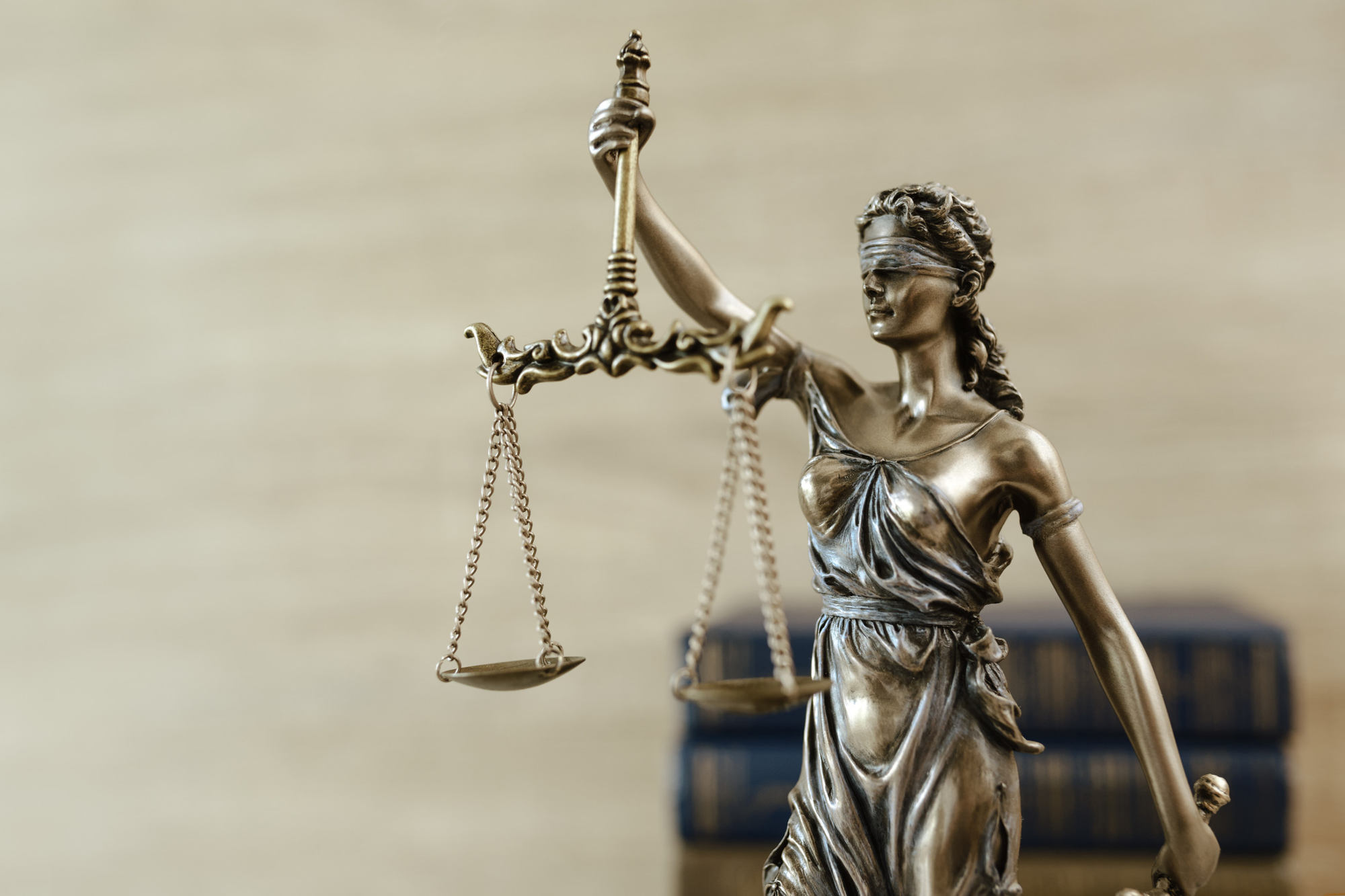 'Lady Justice' statue against blurred background of legal books